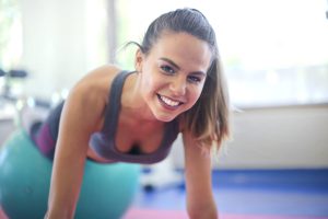 A cheerful woman exercises on a stability ball indoors, embodying fitness and a healthy lifestyle.